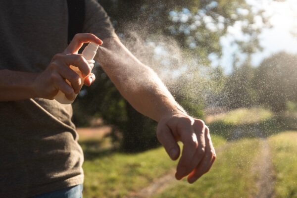 Persoană aplicând spray repelent pe braț afară